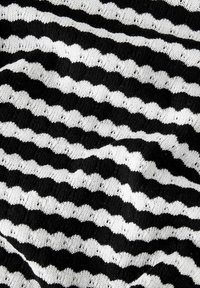 Schwarz-weißer Strickstoff mit wellenförmigen Streifen. Das strukturierte Muster erzeugt wechselnde feste und offene Abschnitte über die Oberfläche.