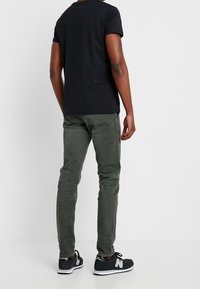 Černé tričko s krátkým rukávem, olivově zelené slim-fit kalhoty a černé sportovní boty s bílými detaily. Hladká textura, ležérní design.