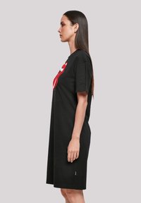Schwarzes Baumwoll-T-Shirt-Kleid mit lockerer Passform, das ein auffälliges Design von roten und weißen Lippen auf der Vorderseite aufweist. Mit kurzen Ärmeln und knielanger Länge.