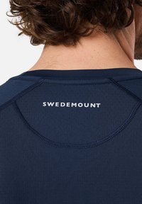 Mørkeblå træningsskjorte med mesh-struktur, med rund halsudskæring og "SWEDEMOUNT" logo i hvidt på den øverste del af ryggen.