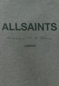 Grön sweatshirt i texturerad tyg med bold "ALLSAINTS" text och mindre text som säger "London" nedan. Enkelt design.