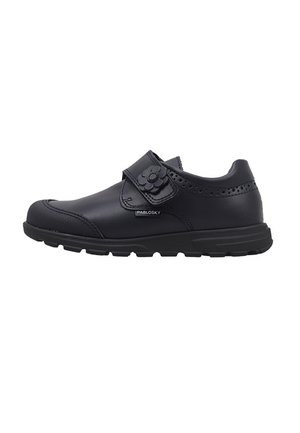 Zapato infantil de cuero negro con correa de velcro y detalle de flor. Presenta acentos perforados y una suela de goma texturizada para mayor agarre.