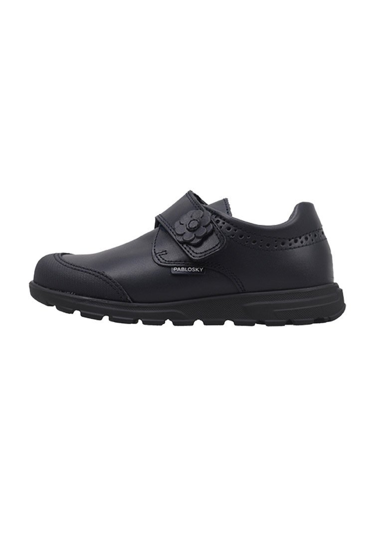 Zapato infantil de cuero negro con correa de velcro y detalle de flor. Presenta acentos perforados y una suela de goma texturizada para mayor agarre.