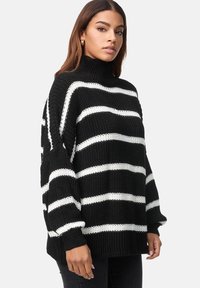 Maglione a righe bianche e nere in maglia, con colletto alto, vestibilità over e polsini a coste. La texture sembra spessa e calda.