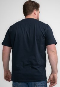 Camiseta de algodón azul marino de manga corta, con cuello redondo y una textura suave, combinada con unos vaqueros azules deslavados. La vista desde atrás muestra simplicidad.