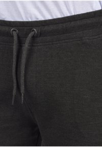 Pantalons de jogging gris foncé en tissu texturé, dotés d'une taille élastique avec cordon de serrage et extrémités de cordon métalliques.