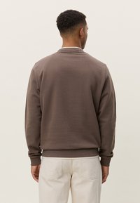 Sweat-shirt marron à encolure ronde simple, manches longues et poignets côtelés. Texture lisse, coupe décontractée, sans logo ni motif visible.