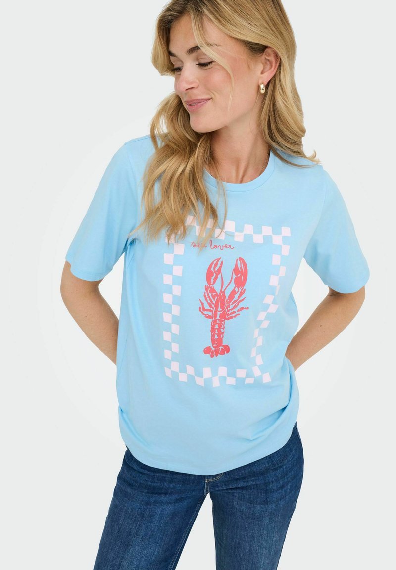 Lichtblauwe katoenen t-shirt met een rode kreeftgrafiek en een roze geblokte rand. Korte mouwen, relaxte pasvorm. Gecombineerd met donkerblauwe jeans.