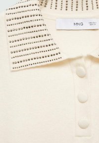 Cremfarbendes Strickshirt mit einem mit Nieten besetzten spitzen Kragen und drei mit Stoff bedeckten Knöpfen an der vorderen Leiste.