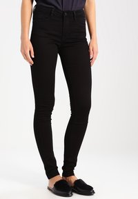 Svarta slim fit jeans med en slät yta, medelhög midja och klassisk femfickdesign. Matchas med svarta platta skopåsliven.