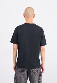 T-shirt en coton noir avec un col rond et des manches courtes, vu de dos. Présente une coupe décontractée et un minimum de détails.