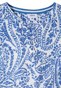 Blouse blanche avec un motif floral cachemire bleu complexe, col en V et étiquette avec l'inscription "CECIL" sur le col intérieur.