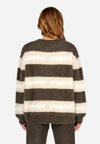 Ριγέ oversized πουλόβερ από μαλακό, αφράτο υλικό. Διαθέτει σκούρες καφέ και κρεμ ρίγες με επαναλαμβανόμενο μοτίβο κειμένου. Μακρυά μανίκια και στρογγυλή λαιμόκοψη.