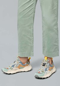 Las zapatillas multicolores presentan un diseño floral, materiales de ante y malla, una suela gruesa y detalles amarillos en el talón y la lengua.