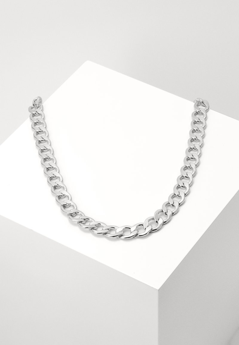 Colar de corrente de prata com grandes elos lisos, acabamento brilhante e fecho redondo, colocado contra um fundo branco minimalista.