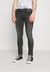 Mörkgrå tajta jeans med en slät struktur, femficksdesign och uppvikta fållar, kombinerade med svarta höga sneakers.