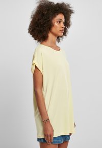 Løs pasform gul T-shirt lavet af blødt bomuld. Har en bred halsudskæring og korte opsmøgte ærmer, med en glat tekstur og afslappet design.