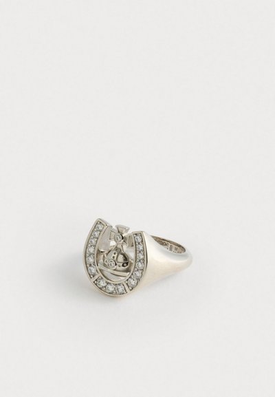 Bague en argent en forme de fer à cheval, ornée de petits gemmes clairs le long du bord extérieur et d'un motif central représentant une croix.