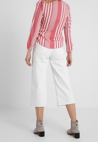 Gestreifte rosa Bluse mit langen Ärmeln, kombiniert mit weißen kürzeren Hosen. Graue Knöchelstiefel mit Nietenakzenten.