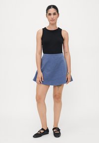 Svart ermeløs topp kombinert med en A-linjeet blå denimskjørt med frynsete kant. Modellen har på seg svarte flate sko.
