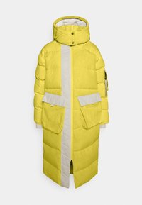 Keltainen toppatakki, jossa on harmaa keskiosa, suuret etutaskut ja korkea kaulus, jossa painonapit. Pehmeä, tikattu pinta.