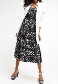 Black and white patterned dress with a flowing skirt, paired with a white blazer. The model wears black platform heels.