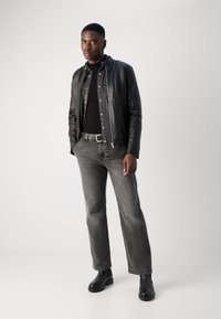 Zwarte leren jas over een zwart shirt, grijze jeans en zwarte enkellaarsjes. De outfit heeft een moderne snit en een minimalistisch ontwerp.