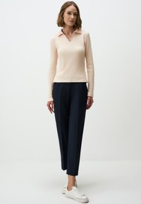 Lichtroze, gestructureerde lange mouw top met V-hals en kraag, gecombineerd met hoge taille marineblauwe broeken en witte sneakers.