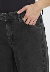 Mustad lõdva lõikega teksapüksid, mis on varustatud ees taskutega, nööpkinnitusega ning kangale õrnade pleekimise detailidega.