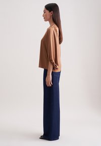 Brun, kortærmet bluse med løs pasform og samling på ærmerne, parret med højtaljede, brede mørk denim jeans.