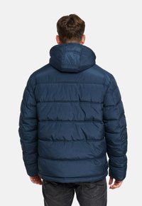 Giacca a vento imbottita blu navy con design trapuntato, cappuccio e polsini elasticizzati. Tessuto liscio con vestibilità comoda e orlo arrotondato.