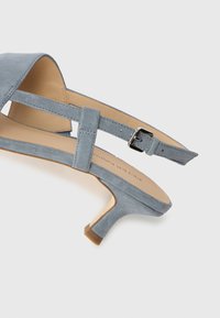 Blue suede high-heeled sandal with an open toe, adjustable ankle strap, and a subtle textured finish. Minimalist design with a tapered heel.