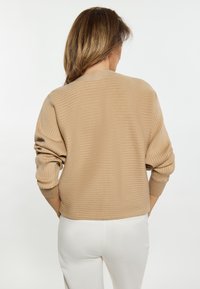 Beige geribde trui met een ronde halslijn en een aansluitend ontwerp. Lange mouwen met opgerolde manchetten. De trui heeft een soepele textuur.