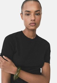 Black short-sleeve t-shirt. Transparent green bangle on wrist. Smooth texture. Clean lines, close-fitting design. Neutral background.