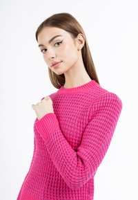Maglione a maglia fucsia con un motivo testurizzato e polsini a costine. Design aderente con scollatura a girocollo e maniche lunghe.