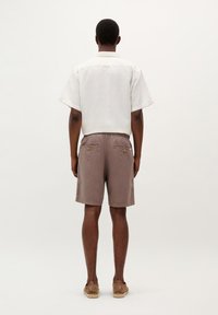 Kortærmet hvid tekstureret skjorte og brune shorts med baglommer og knapdetaljer. Styllet med lysebrune sko.
