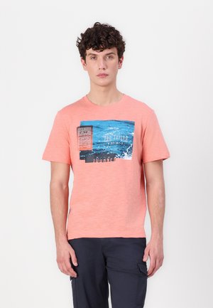 T-shirt corail à manches courtes avec une finition texturée, affichant un imprimé graphique en bleu et noir avec un texte superposé. Encolure ras du cou.