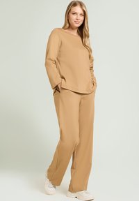 Top beige de manga larga con escote redondo y ajuste relajado, combinado con pantalones anchos a juego. Textura suave y diseño minimalista.