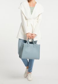 Jasnoniebieska skórzana torebka w strukturalnym kształcie z podwójnymi uchwytami, w połączeniu z kremową kurtką i jasnoniebieskimi dżinsami.