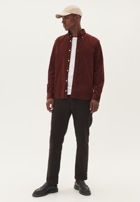Bordeaux corduroy overhemd, witte t-shirt met ronde hals eronder, zwarte broek, beige pet en zwarte schoenen; gladde stof met knoopdetails.