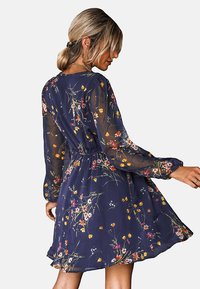 Marinebloemige jurk van lichtgewicht, doorschijnende stof. Kenmerkt lange, gathered mouwen, een getailleerde taille en een zwierige rok met kleurrijke bloempatronen.