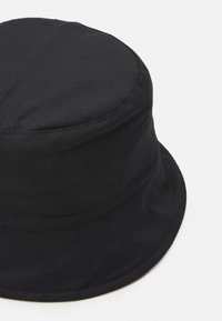 Chapéu preto de balde feito de algodão, com uma coroa redonda e estruturada e um aba larga e macia. Textura suave com detalhes de costura limpa.