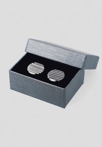 Okrągłe, srebrne spinki do mankietów z wytłaczanym wzorem w paski, umieszczone w szarej, teksturowanej walizce wyłożonej czarnym aksamitem z otwartą pokrywką.