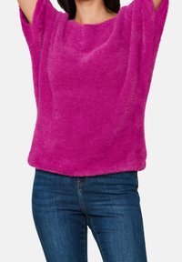 Luddig, ljusrosa topp med vida ärmar och avslappnad passform, tillverkad av mjukt tyg. Parat med mörkblå jeans.