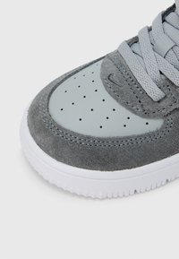 Sivá teniska z brúsených a kožených materiálov, s okrúhlou špičkou, perforovaným dizajnom a bielou gumovou podrážkou s textúrovaným gripom.