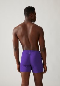 Paarse katoenen boxershorts met een elastische tailleband, gezien van de achterkant. Soepele textuur, aansluitend ontwerp en minimale merkdetails.