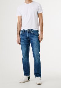 Vit bomull t-shirt med liten logotyp, blå denim jeans med lätt blekning, regular fit, och vita sneakers med gröna accenter.