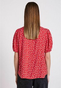Blusa rossa a fiori con maniche a palloncino corte, vista posteriore che mostra un orlo dritto e piccoli motivi floreali bianchi su tessuto leggero.