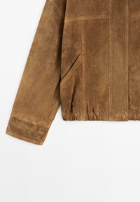 Bruine suède jas met lange mouwen, diagonale zijzak, gestikte details, elastische zoom en drukknoopsluiting aan de voorkant.