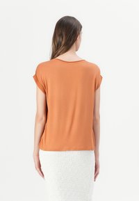 Camiseta de manga corta, de color naranja, con un corte cómodo, textura suave y un escote redondeado, combinada con una falda blanca texturizada.